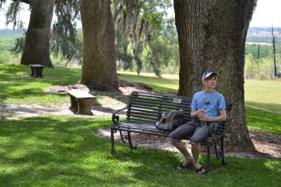 Lisa sits on a bench in the shade of the oak trees at Bok Tower Sanctuary, Florida.